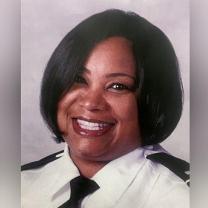 Head shot of black woman with short black hair smiling wearing a police uniform