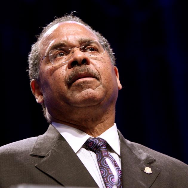 Black man in a suit with glasses speaking with his head tilted back